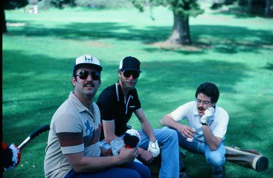 Three friends relax on the grass in a park, enjoying drinks and each other's company on a sunny day.