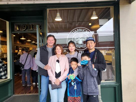 Group of family members smiles at the entrance of a coffee shop in Seattle on a bustling day.