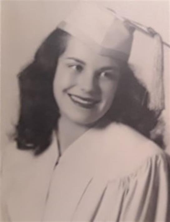 A cheerful young woman in a graduation cap and gown beams at the camera with confidence and joy.