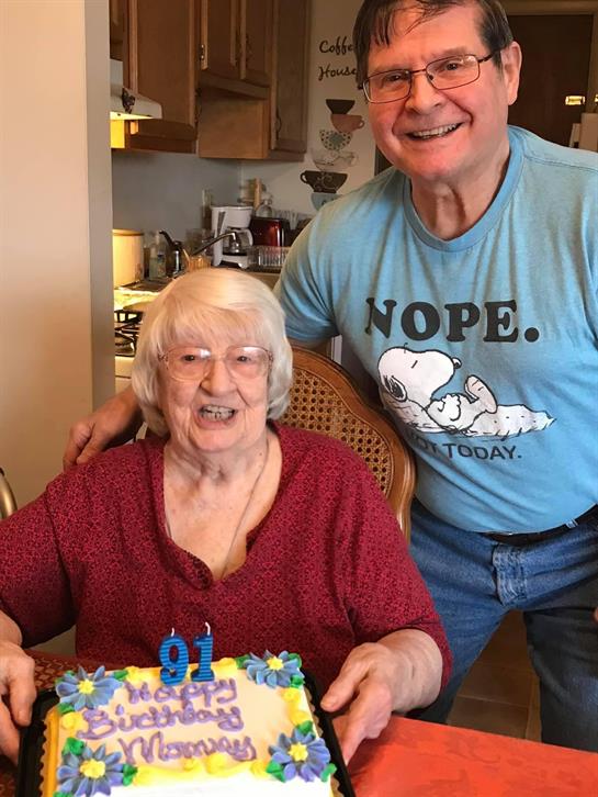 Family gathers to celebrate a joyful 91st birthday with cake and smiles in a warm home environment.