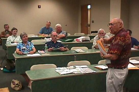 Senior adults attentively participate in a workshop held in a classroom with tables and chairs.