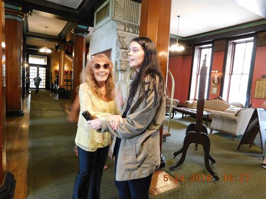 Two women share laughter in a spacious lobby filled with vintage decor and natural light.