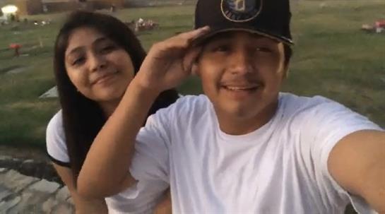 Two friends smile and pose together in a park filled with greenery under a clear blue sky.