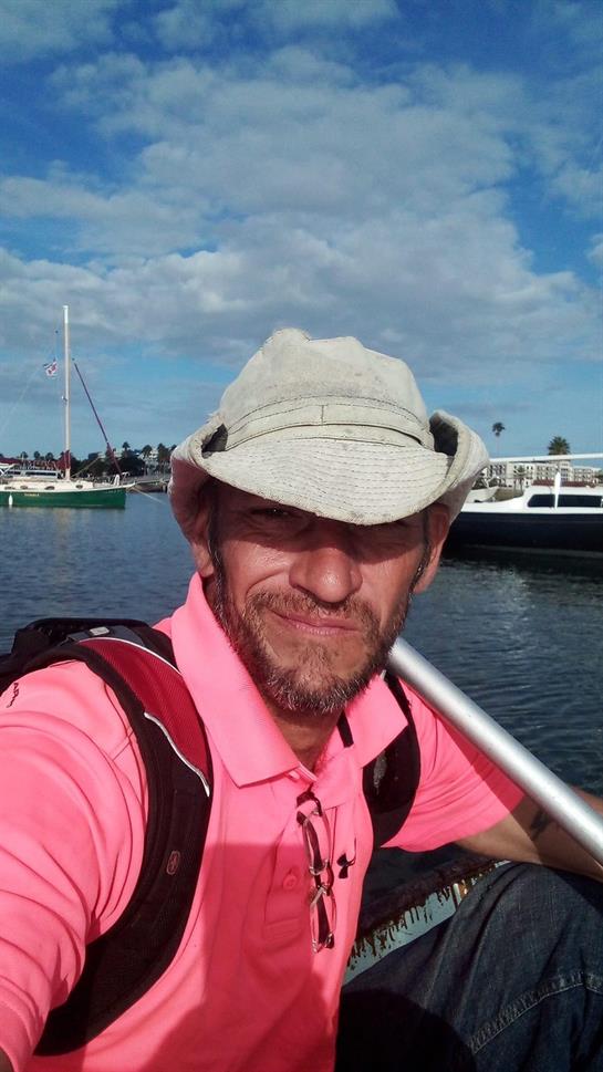 A man with a hat smiles while paddling a boat in the marina, enjoying the beautiful weather.