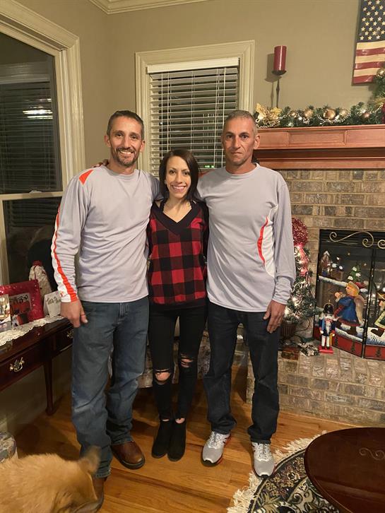 Three individuals pose together in a warmly decorated living room, celebrating the holidays.