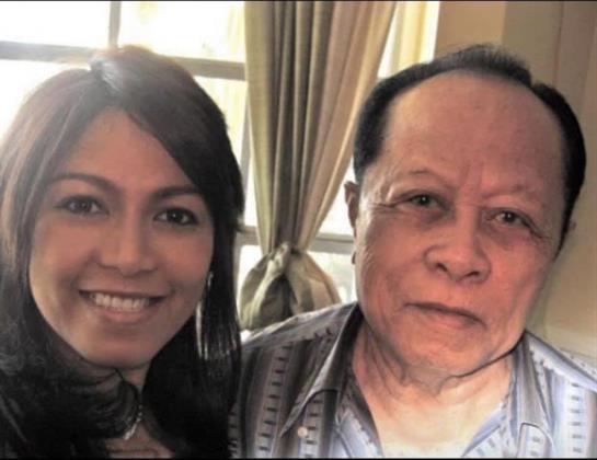 Cheerful woman stands next to an older gentleman in a bright, relaxed environment.