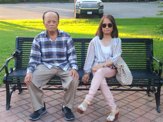 Two individuals relax on a bench in a park, enjoying each other's company under the sun.