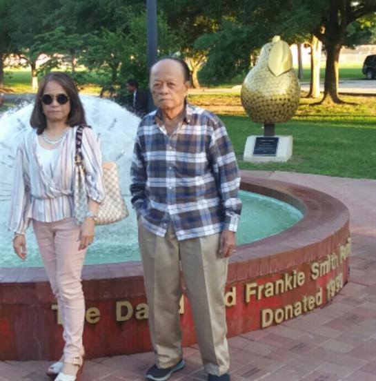 Couple poses near a decorative fountain in a park as sunlight casts warm tones around them.