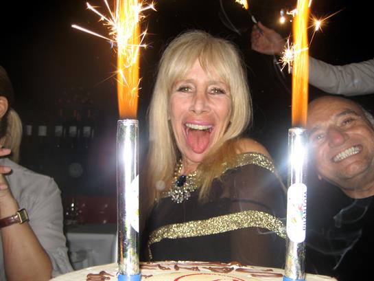 A woman celebrates her birthday joyfully with cake and sparklers while friends cheer around her.