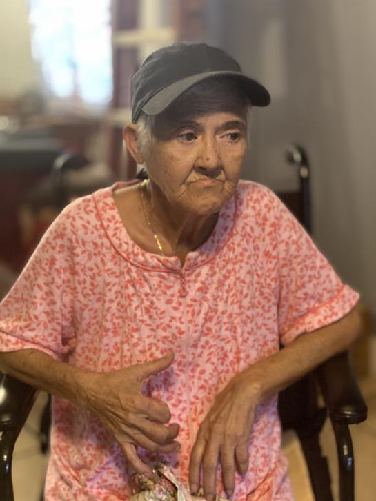 Senior woman in casual attire sitting comfortably in her wheelchair, looking thoughtful.