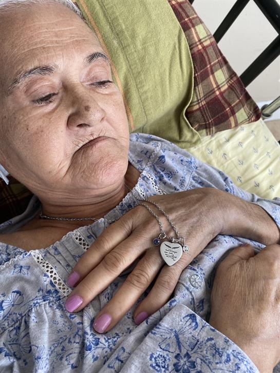 An elderly woman lies in bed, wearing a blue patterned blouse, showing calmness and tranquility.