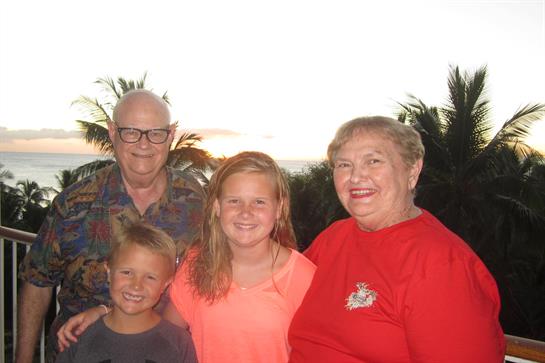 Family poses together with smiles as the sun sets over a tropical landscape.