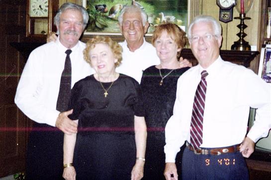 A group of five adults dressed in black clothes standing together, sharing smiles in a cozy setting.