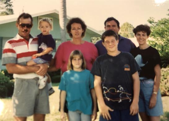 A joyful family poses together outdoors, showcasing warmth and unity under bright sunlight.