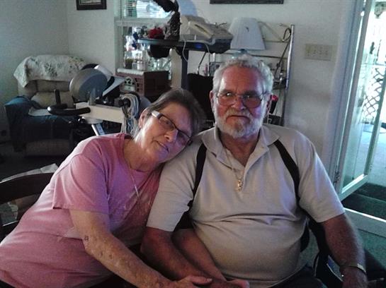 A couple sits closely together in their living room, smiling and enjoying each other's company.
