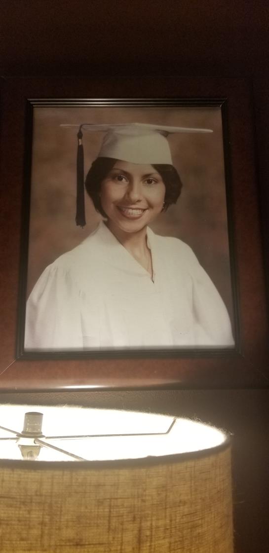 A young woman proudly wears her graduation cap and gown, smiling warmly at the camera.