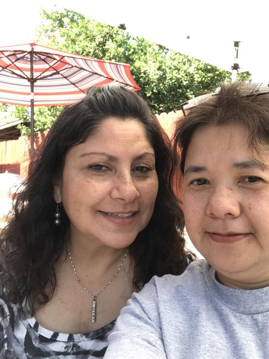 Two women share smiles while enjoying a sunny day outdoors at a cafe with umbrellas.