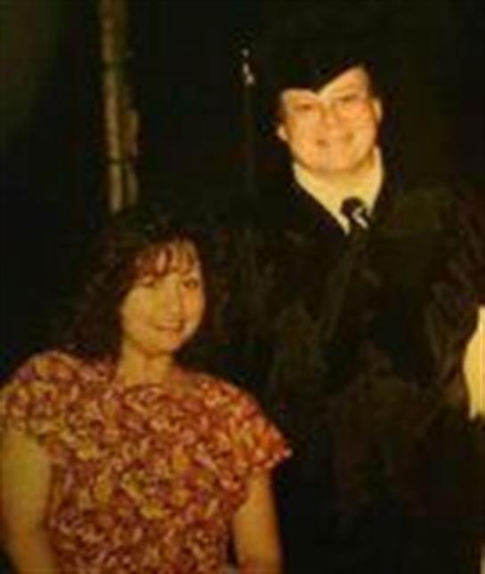 Two individuals celebrating a graduation, one in a cap and gown, and a relative smiling beside them.
