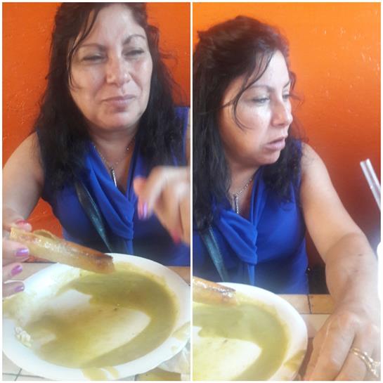 A woman seated at a table tastes food, expressing delight against a colorful backdrop.