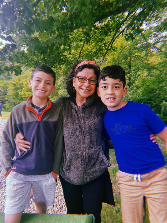 Two boys stand beside a woman, smiling while enjoying a beautiful sunny afternoon in the park.