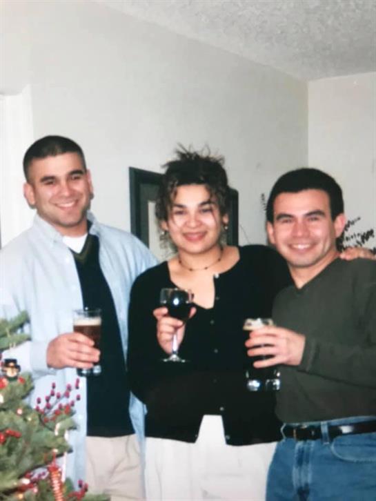 Three friends hold drinks and smile together, enjoying a cozy winter gathering in a warmly lit room.