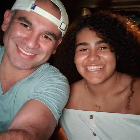 A father and daughter share joyful smiles while dining out in a relaxed setting at night.