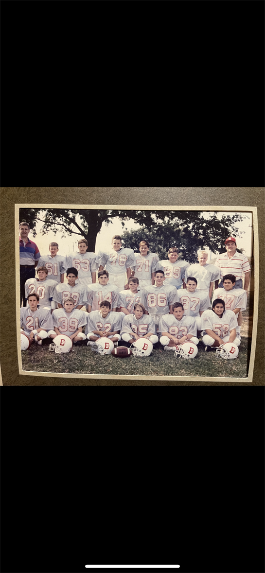 Young athletes in gray uniforms gather for a group photo on a sunny day at the field.