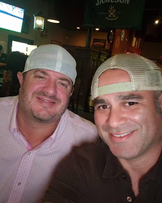 Two men pose together, smiling happily while enjoying the vibrant atmosphere of a bar.