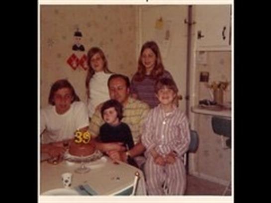 A family celebrates a birthday together with cake and smiles in a warm home environment.