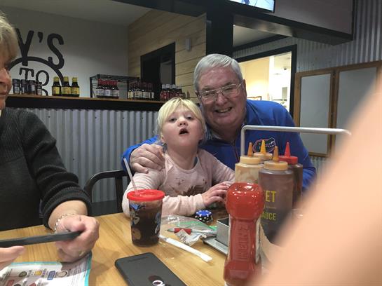 A joyful grandfather and his granddaughter share a meal at a diner, smiling and having fun.