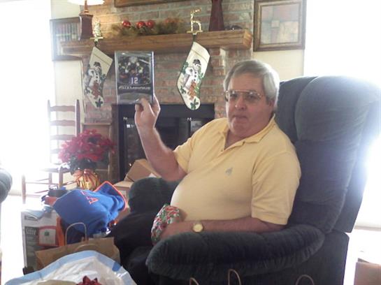 Man in a yellow shirt sits relaxed, holding an object while surrounded by holiday decorations.