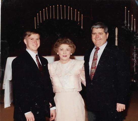 Three formally dressed people stand together, smiling, celebrating a special occasion.