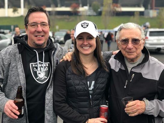 Group of friends smile together while tailgating at a football stadium on a chilly day.
