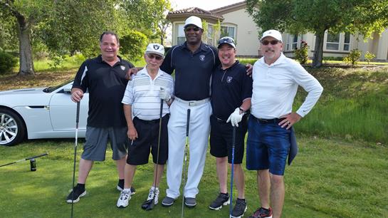 Five friends posing together on a golf course, enjoying a day outdoors under clear skies.