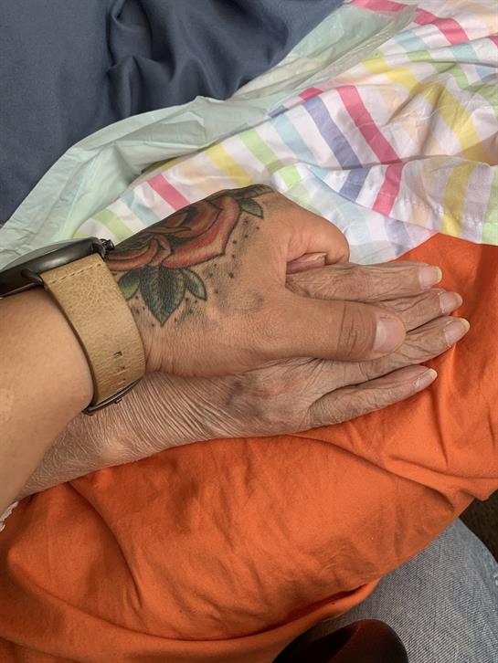 Two hands, one young and tattooed, the other aged, touch in a warm display of affection.