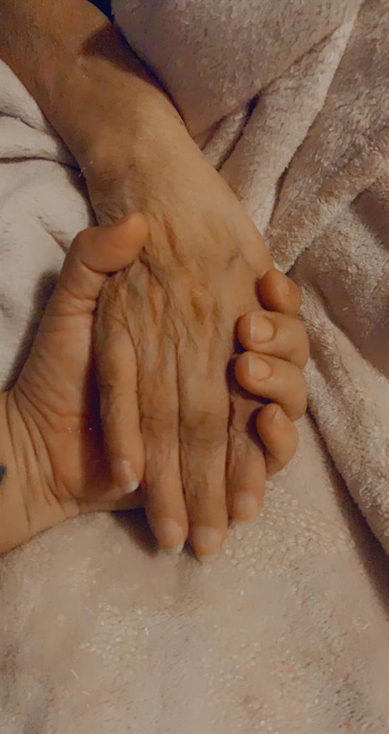 Two hands, one aged and one younger, hold each other, representing love and connection.
