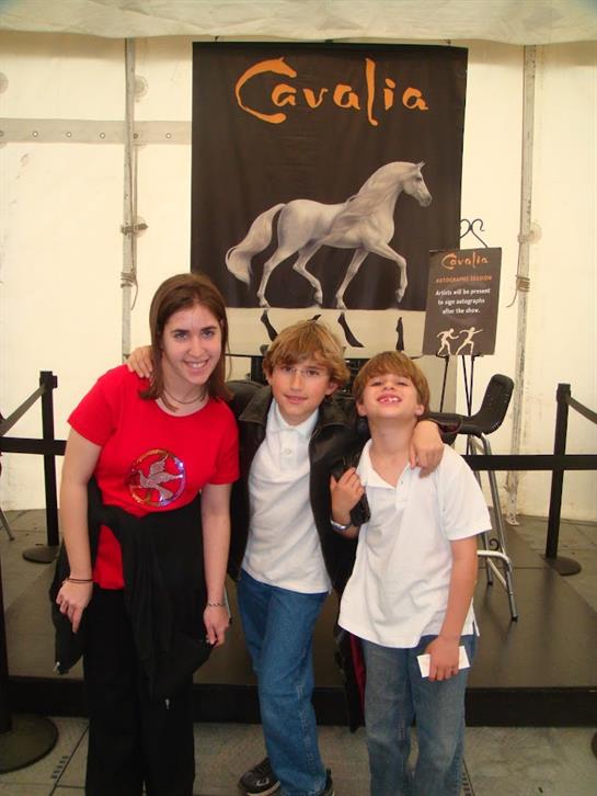 Three smiling children pose with joy at the Cavalia equestrian event, surrounded by banners.