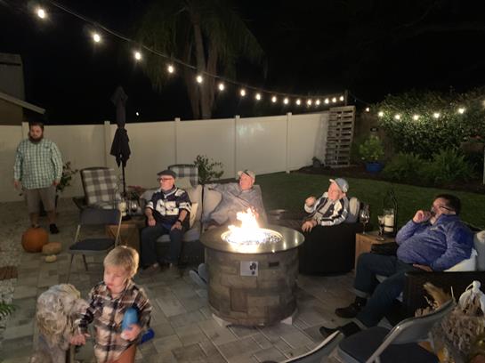Loved ones share stories and laughter near a cozy fire pit under string lights in the backyard.