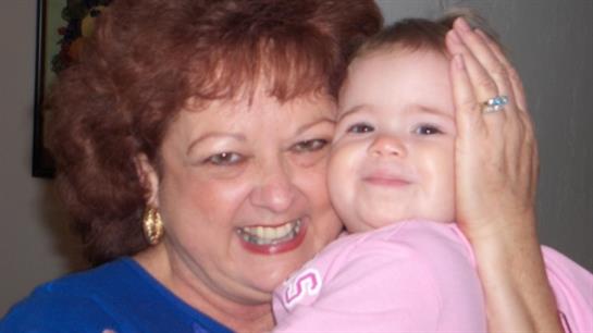 A cheerful grandmother holds her granddaughter, both smiling joyfully in a loving moment.