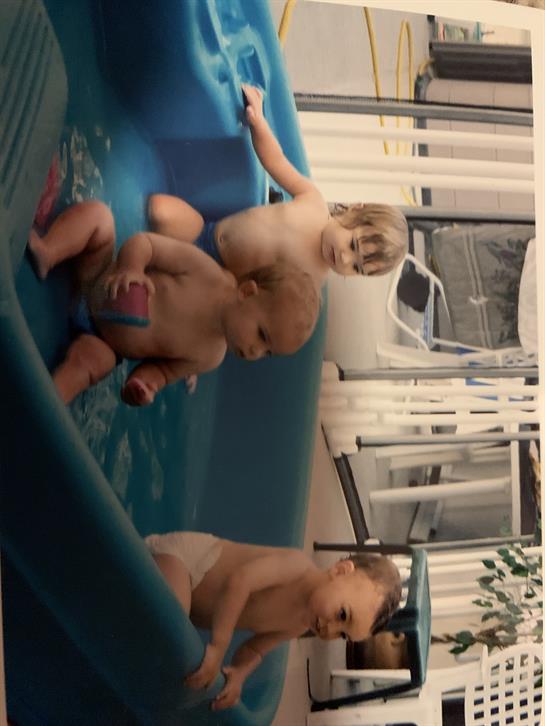 Three children enjoy splashing and playing in a bright inflatable pool on a sunny day.