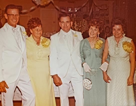 Five friends pose together in formal wear at a lively celebration filled with decorations.