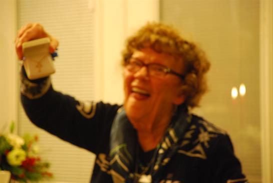 Elderly woman happily raises a party item, sharing joy at a cheerful gathering with friends.