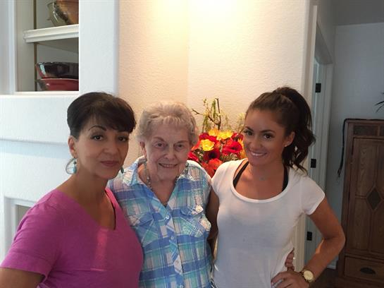 Three women stand together in a brightly lit room, smiling and enjoying each other's company.