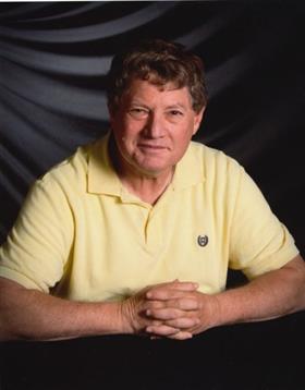 A man poses confidently, smiling warmly while seated against a dark backdrop.