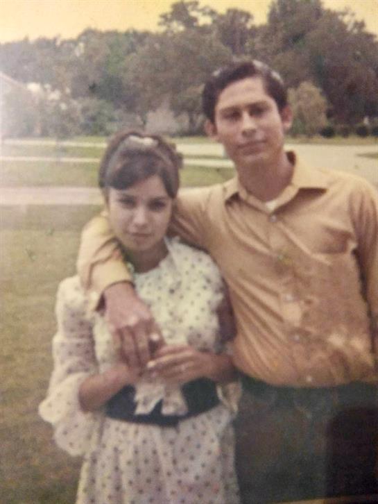 A young couple stands close together in a park, smiling and enjoying their time on a sunny day.