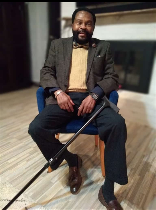 A distinguished elderly man sits comfortably in a chair, showcasing a formal look with a cane.