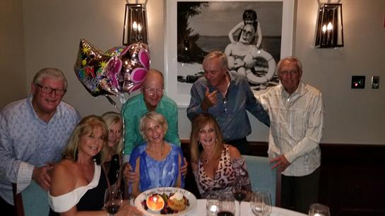 A group of six friends joyfully celebrates together at a restaurant, enjoying dinner and balloons.