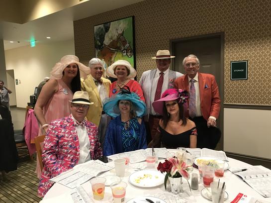 A group of friends dressed in vibrant hats enjoys a festive gathering at a dining table.