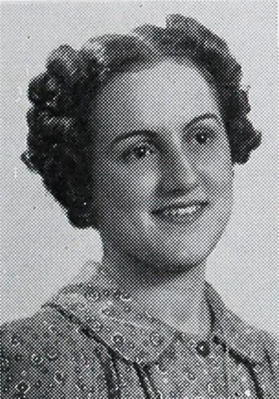 A smiling woman with curly hair in a patterned dress poses for a black-and-white portrait.