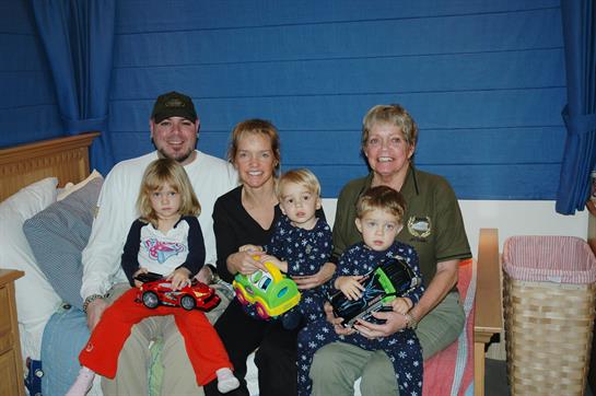 A joyful group of six poses together, children holding colorful toys, smiling in a warm setting.